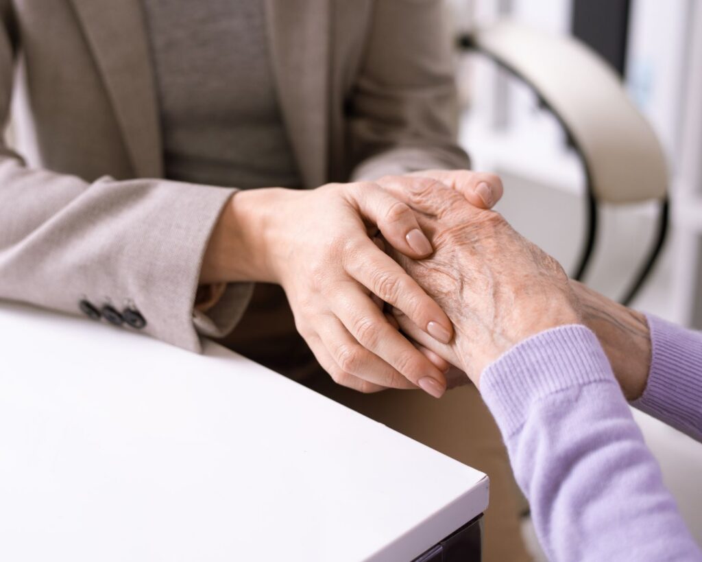 2 elderly people's hands joined over a white table